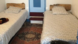 A room with two beds, a wooden headboard, a patterned rug, and a blue door. - La Coquille Napoléon (Uhart-Cize)