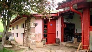 A rustic building with a red door, stone walls, and a stone staircase leading to the entrance. - La Coquille Napoléon (Uhart-Cize)