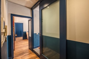 Un pasillo con suelo de madera, una puerta azul y un panel de vidrio.