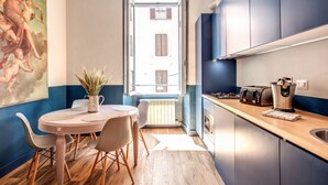 A compact kitchen with a dining area, a window with shutters, and a view of a building outside. - Trastevere Vintage 2 (Rome)