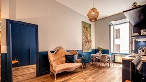 A room with a wooden floor, a sofa, a dining table with chairs, a hanging light fixture, and a large painting on the wall. - Trastevere Vintage 2 (Rome)