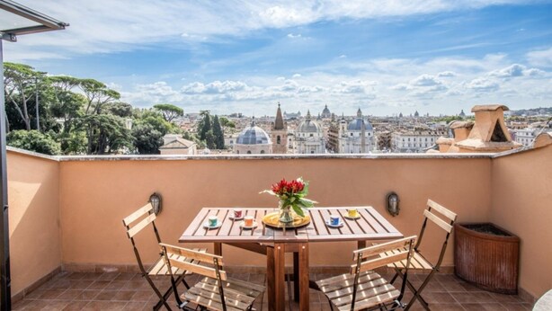 Una terraza con mesa y sillas, un jarrón de flores y vistas a la ciudad.