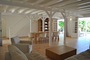 Un espacio habitable amplio con techo alto, estanterías empotradas de madera, una mesa de comedor con sillas y una escalera.