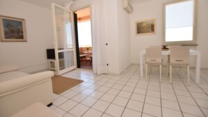 A modern living room with a sofa, a dining table with chairs, a coffee table, and a sliding glass door leading to another room. - Promenade, overlooking the Marciana Marina promenade (Marciana Marina)