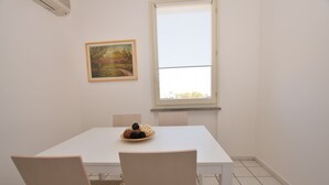 A dining area with a white table and chairs, a painting on the wall, and a window with a view. - Promenade, overlooking the Marciana Marina promenade (Marciana Marina)