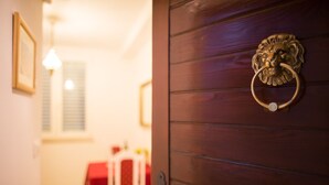 A wooden door with a lion head knocker, a red table, and a white chair in the background. - Apartments Cime (Dubrovnik)