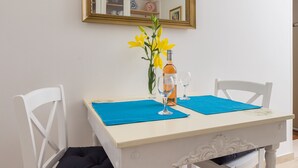 A dining area with a white table, two white chairs, a blue placemat, a vase with yellow flowers, and a wine bottle. - Apartments Cime (Dubrovnik)