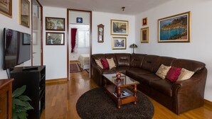 A living room with a brown leather sofa, a glass coffee table, and a flat-screen TV. There are framed pictures on the walls and a plant on the floor. - Apartments Cime (Dubrovnik)
