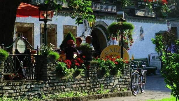 Un bâtiment à la façade en pierre, un vélo garé devant et un drapeau flottant au sommet du toit.