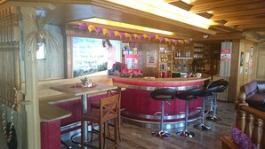 Un espace bar avec un comptoir rouge, des chaises en bois et un plafond en bois.