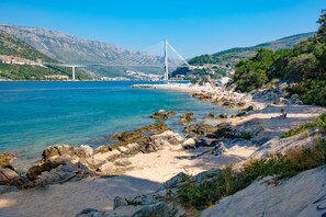 Uma área costeira com uma ponte, praia de pedras e vegetação.