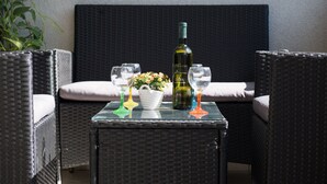 A wicker sofa with cushions, a small table with a bottle of wine, glasses, and a flower vase. - Apartment Filip (Dubrovnik)