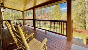 Una terraza de madera con mecedoras y vistas a un área boscosa.