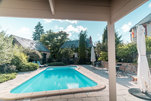 A swimming pool with a stone border, surrounded by a patio area with chairs and umbrellas.