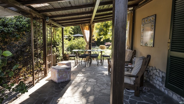 An outdoor patio with stone flooring, wooden tables and chairs, and a covered area with a wooden ceiling. - B&B La Serra (San Miniato)
