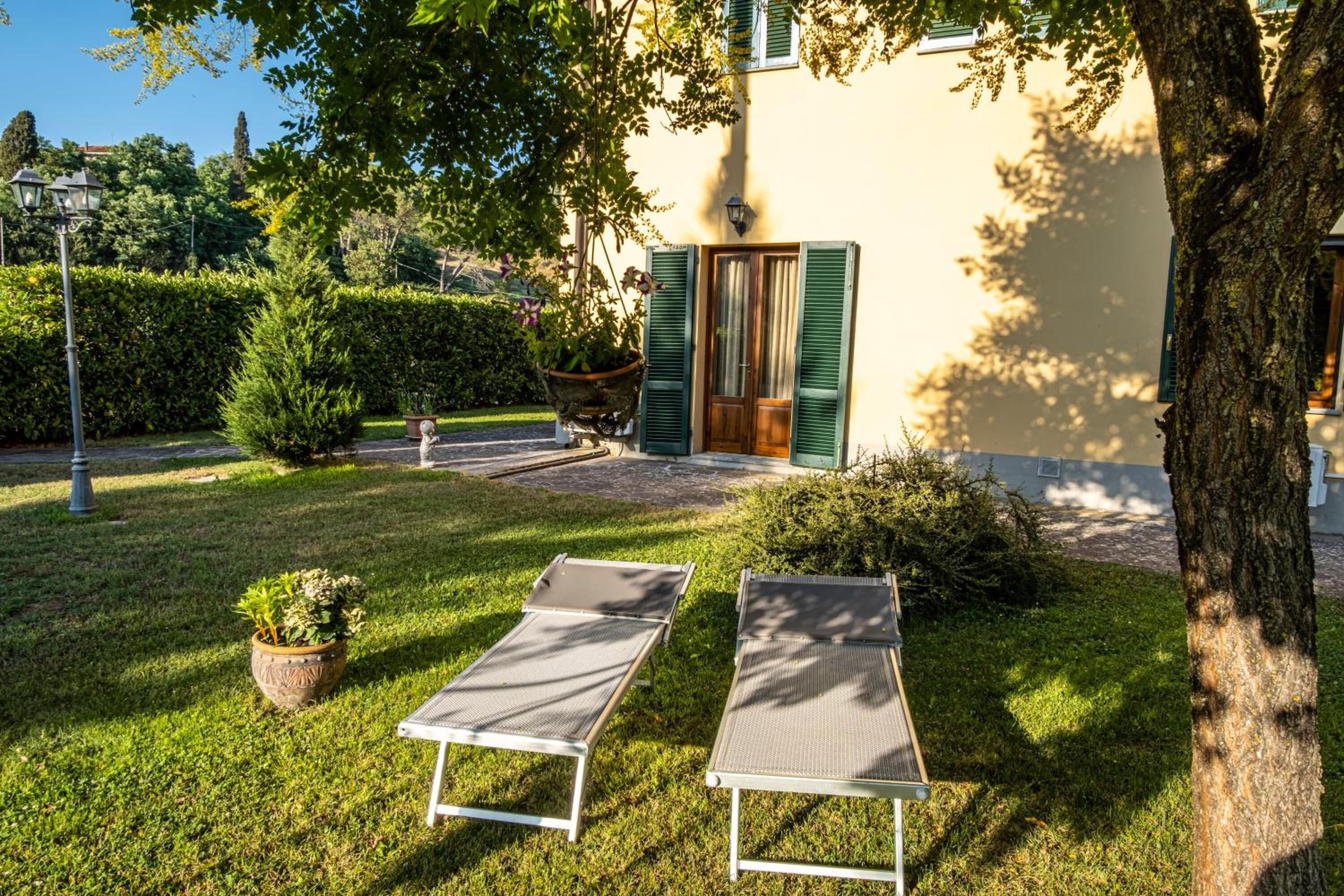 A garden with two sun loungers, a potted plant, and a building with green shutters.
