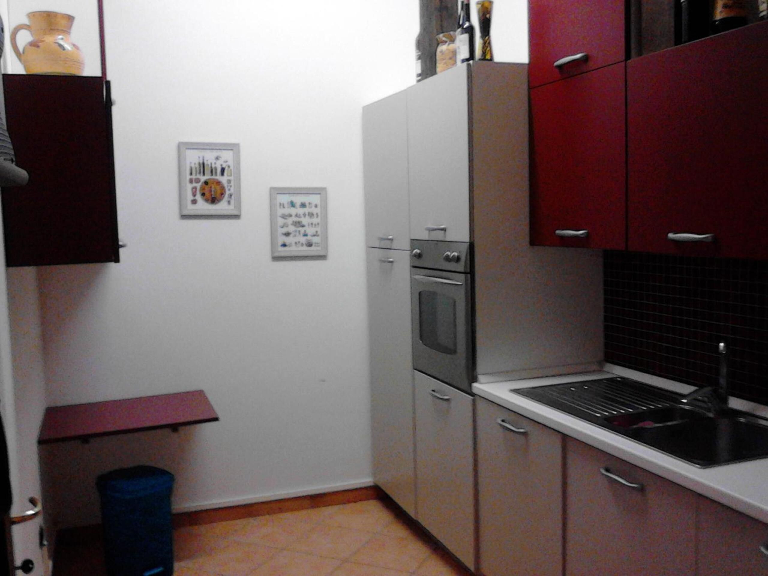 A compact kitchen with white and red cabinets, a built-in oven, and a sink.