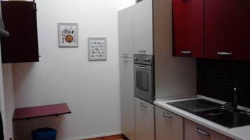 A compact kitchen with white and red cabinets, a built-in oven, and a sink.