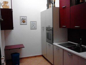 Una cocina compacta con armarios blancos y rojos, un horno empotrado y un lavamanos.