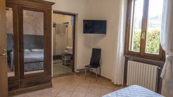 A bedroom with a bed, a wooden wardrobe, a chair, a television, and a window with curtains.
