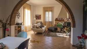 A living room with a sofa, a dining table, and a kitchen area visible through an archway. - B&B La Serra (San Miniato)