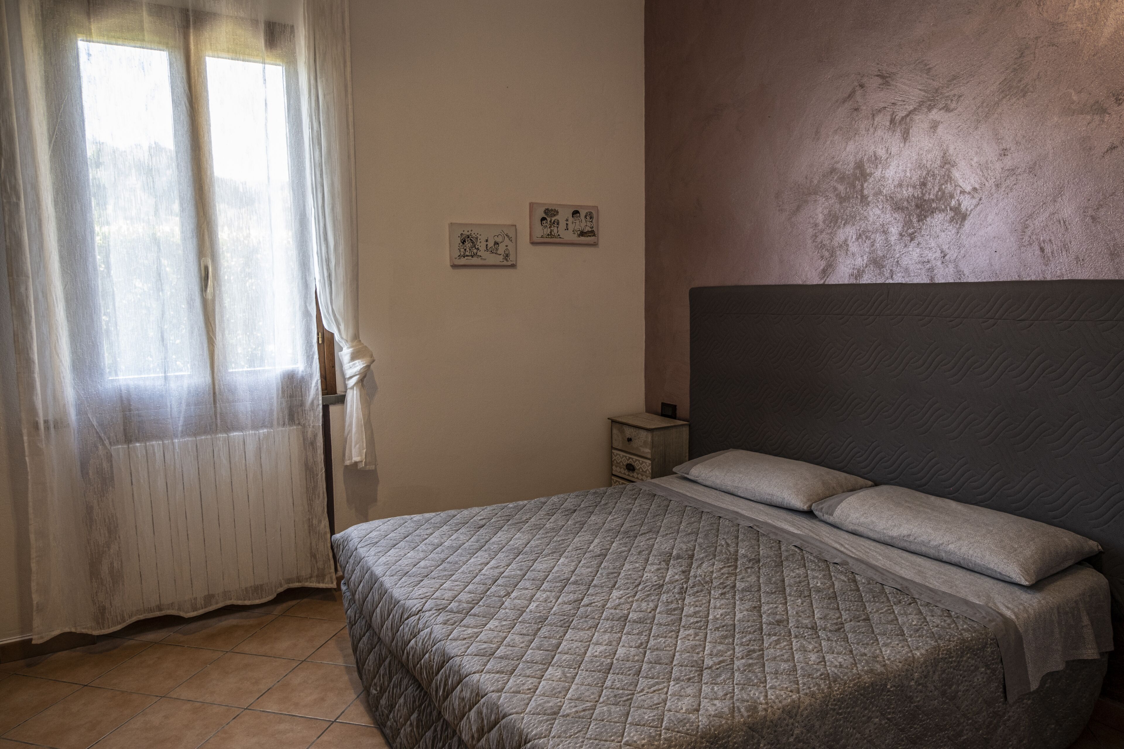 A bedroom with a bed, a nightstand, and two wall-mounted pictures.