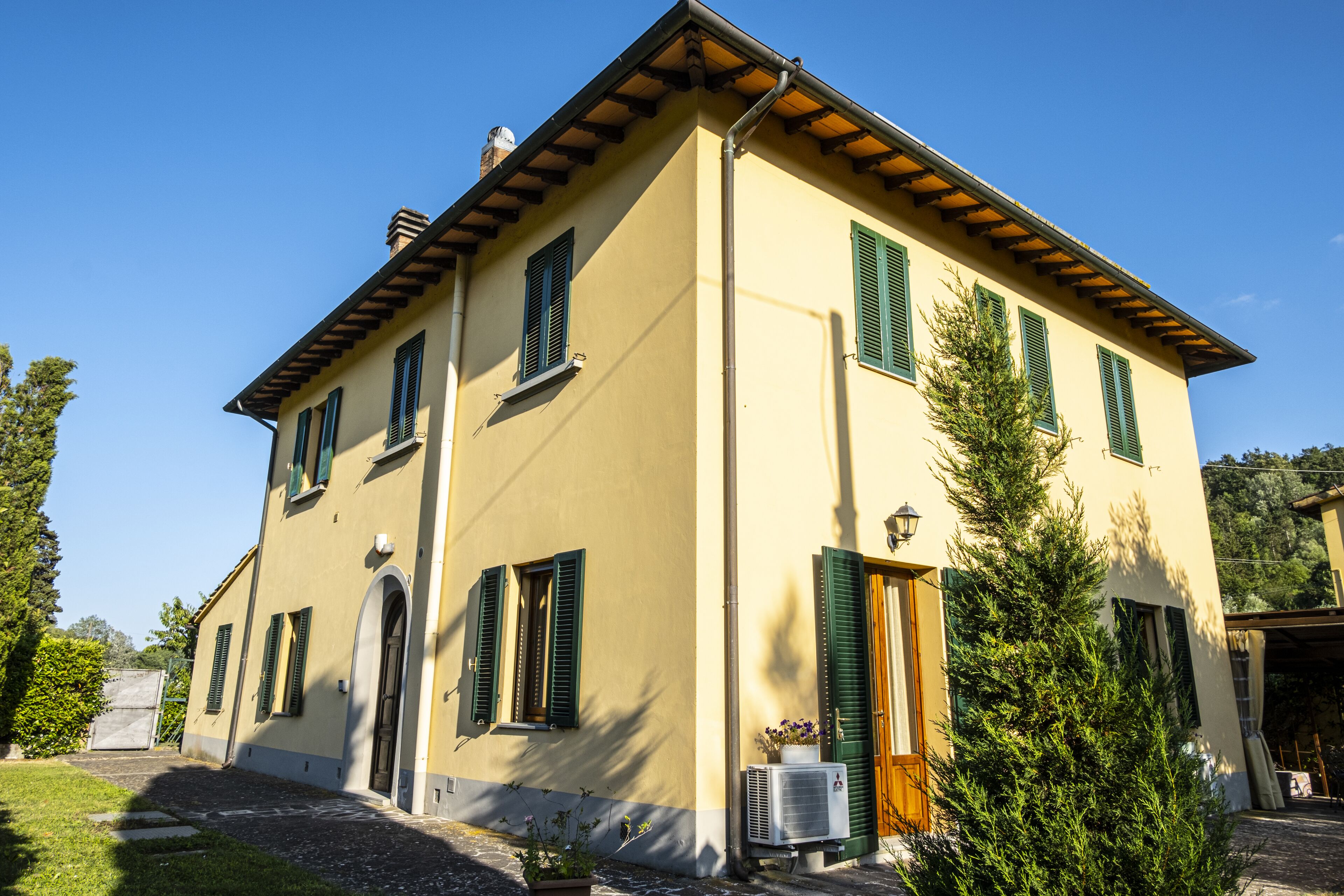 A two-story building with a yellow facade, green shutters, and a chimney.