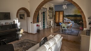 A living room with a sofa, a piano, and a dining area with chairs and a table. - B&B La Serra (San Miniato)