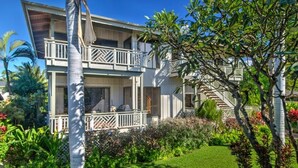 A two-story building with a balcony, surrounded by lush greenery and a well-maintained lawn. - Poipu Beach House: Ocean View, Lush Garden, Beach! (Koloa)