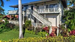 A two-story building with a balcony and a staircase. - Poipu Beach House: Ocean View, Lush Garden, Beach! (Koloa)