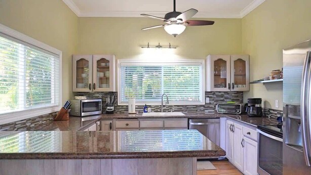 A kitchen with a central island, built-in microwave, stainless steel appliances, and a ceiling fan. - Poipu Beach House: Ocean View, Lush Garden, Beach! (Koloa)
