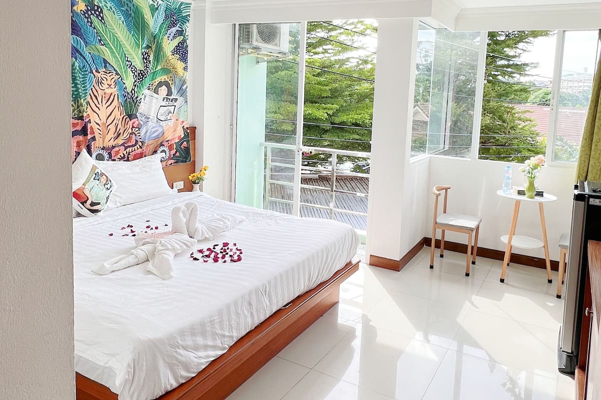 A modern hotel room with a large bed, a balcony with a view, and a colorful mural on the wall.