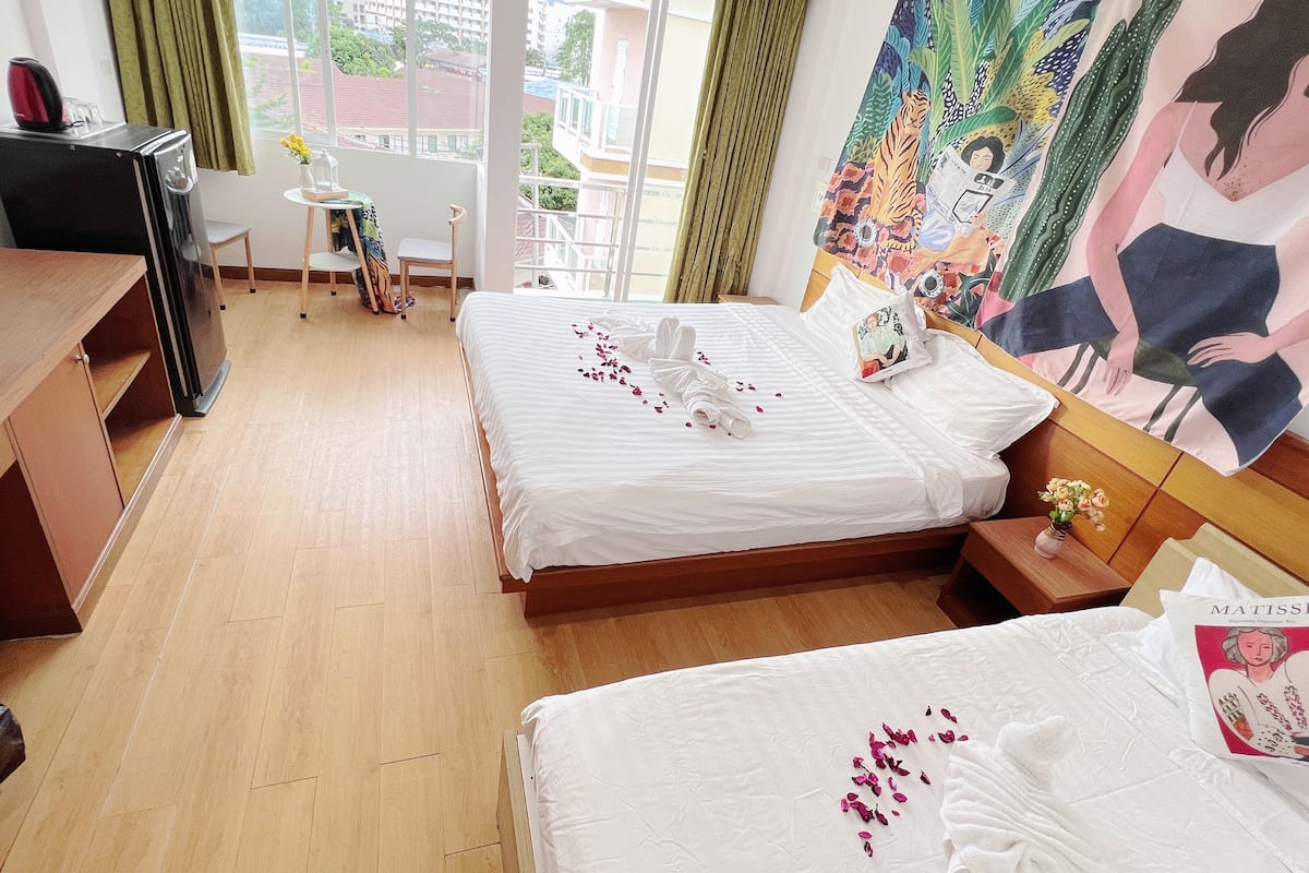 A hotel room with two beds, a desk, a chair, a small table with a vase, and a large painting on the wall.
