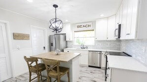 A modern kitchen with white cabinetry, a central island with chairs, a stainless steel refrigerator, and a window with a view of the outdoors. - Golf cart Inc + 4bd/2bth + private pool! (Holmes Beach)