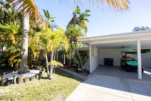 A covered garage with a golf cart, surrounded by palm trees and a white fence.