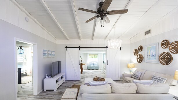 A spacious living room with a ceiling fan, a TV, a sofa, and a dining area in the background. - Golf cart Inc + 4bd/2bth + private pool! (Holmes Beach)