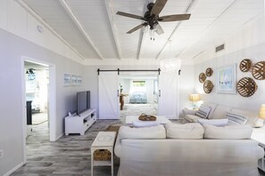 A spacious living room with a ceiling fan, a TV, a sofa, and a dining area in the background. - Golf cart Inc + 4bd/2bth + private pool! (Holmes Beach)