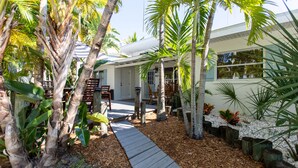 A tropical garden with a wooden pathway leading to a house with a white exterior and large windows. - Golf cart Inc + 4bd/2bth + private pool! (Holmes Beach)
