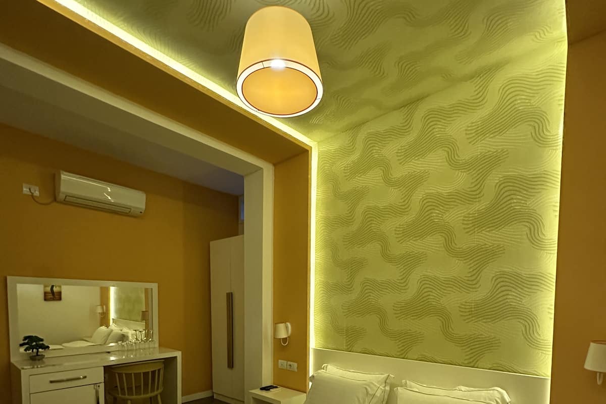 Quarto de hotel com uma cama grande, uma escrivaninha, uma cadeira, um espelho e ar condicionado fixado na parede.