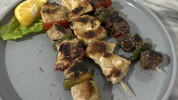 A plate of grilled chicken skewers with vegetables and a slice of lemon on a marble table.
