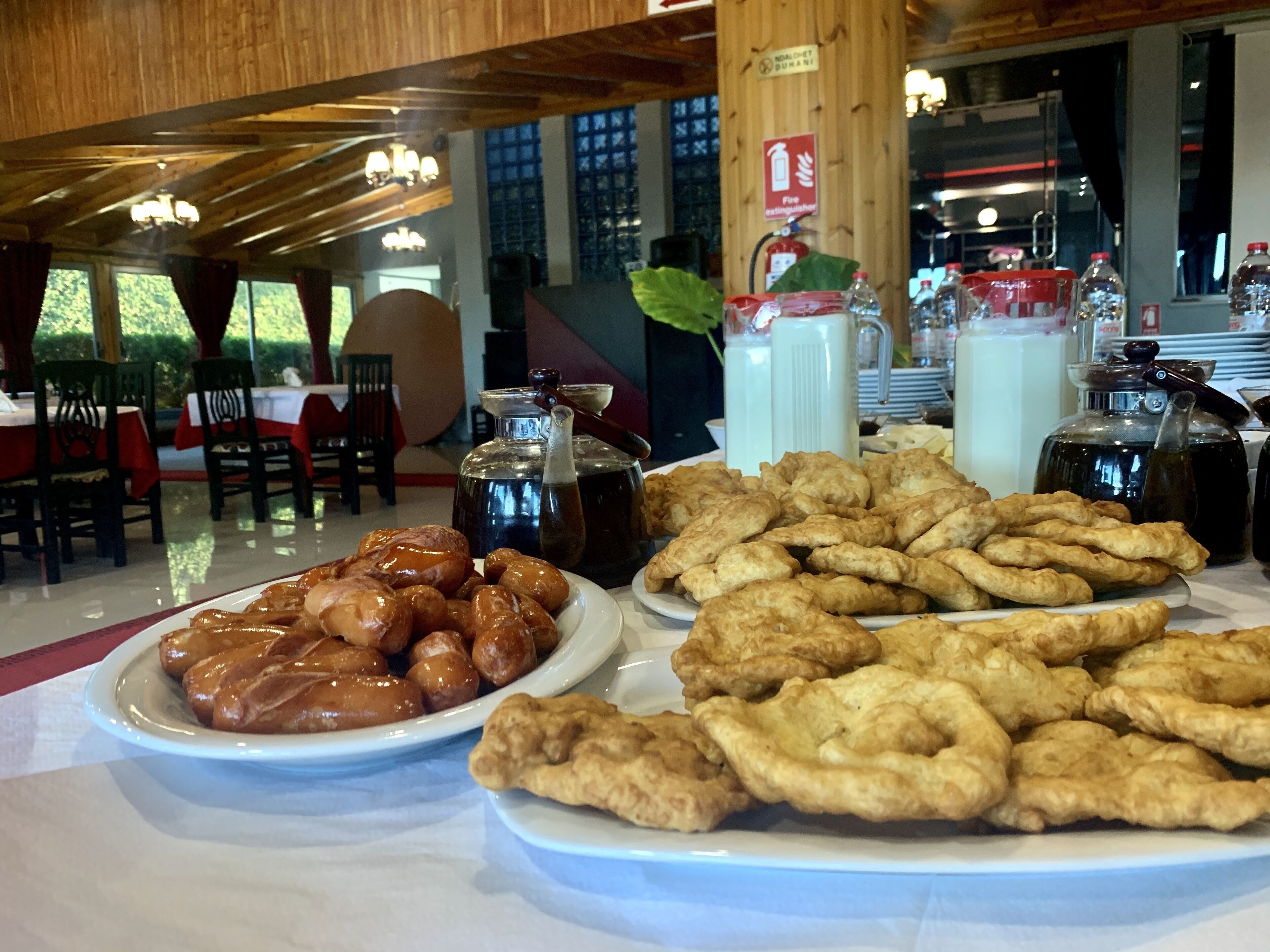 A dining area with wooden ceiling beams, tables with red and white tablecloths, and plates of fried dough pastries.