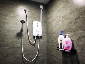 A bathroom with a shower, a white electrical outlet, and two bottles of hair care products on a shelf.