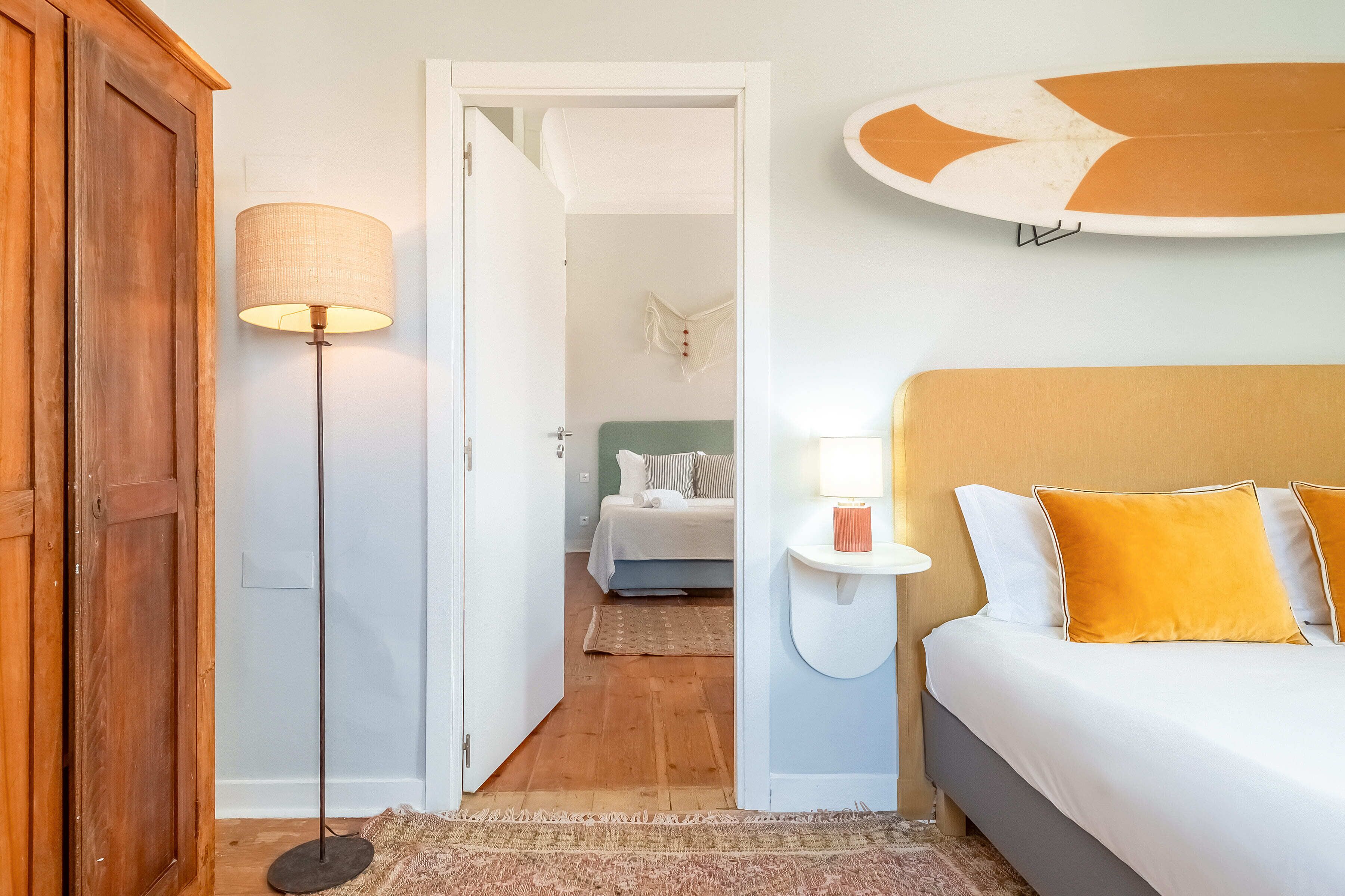 A bedroom with a bed, bedside lamp, and a view into another room.