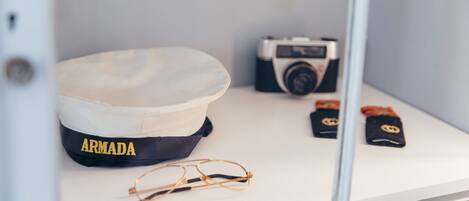A display case containing a navy blue and white cap labeled "ARMADA," a vintage camera, a pair of eyeglasses, and two black patches with yellow emblems.