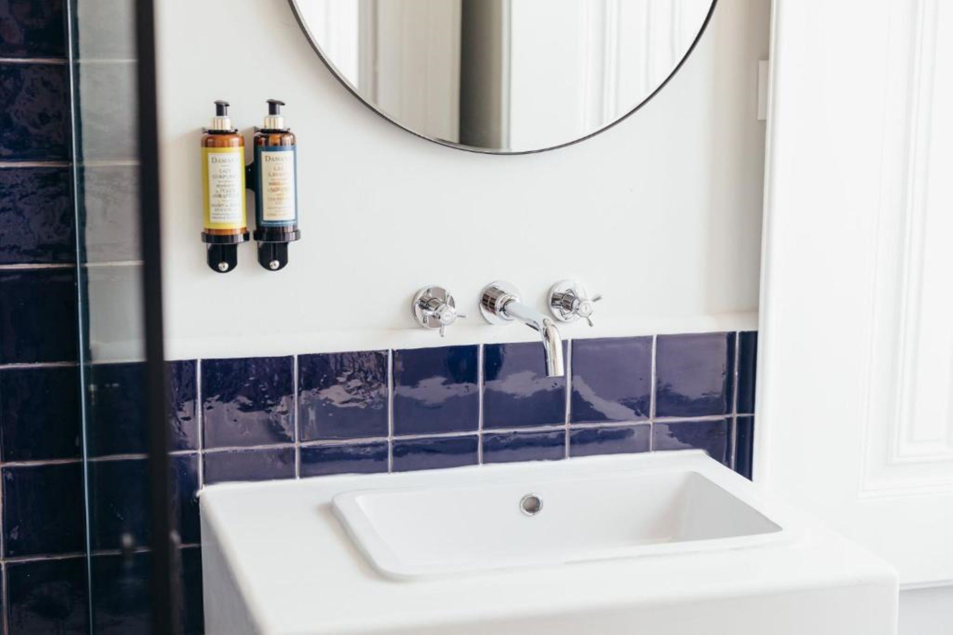 A bathroom with a white sink, two bottles of shampoo, and a mirror above the sink.