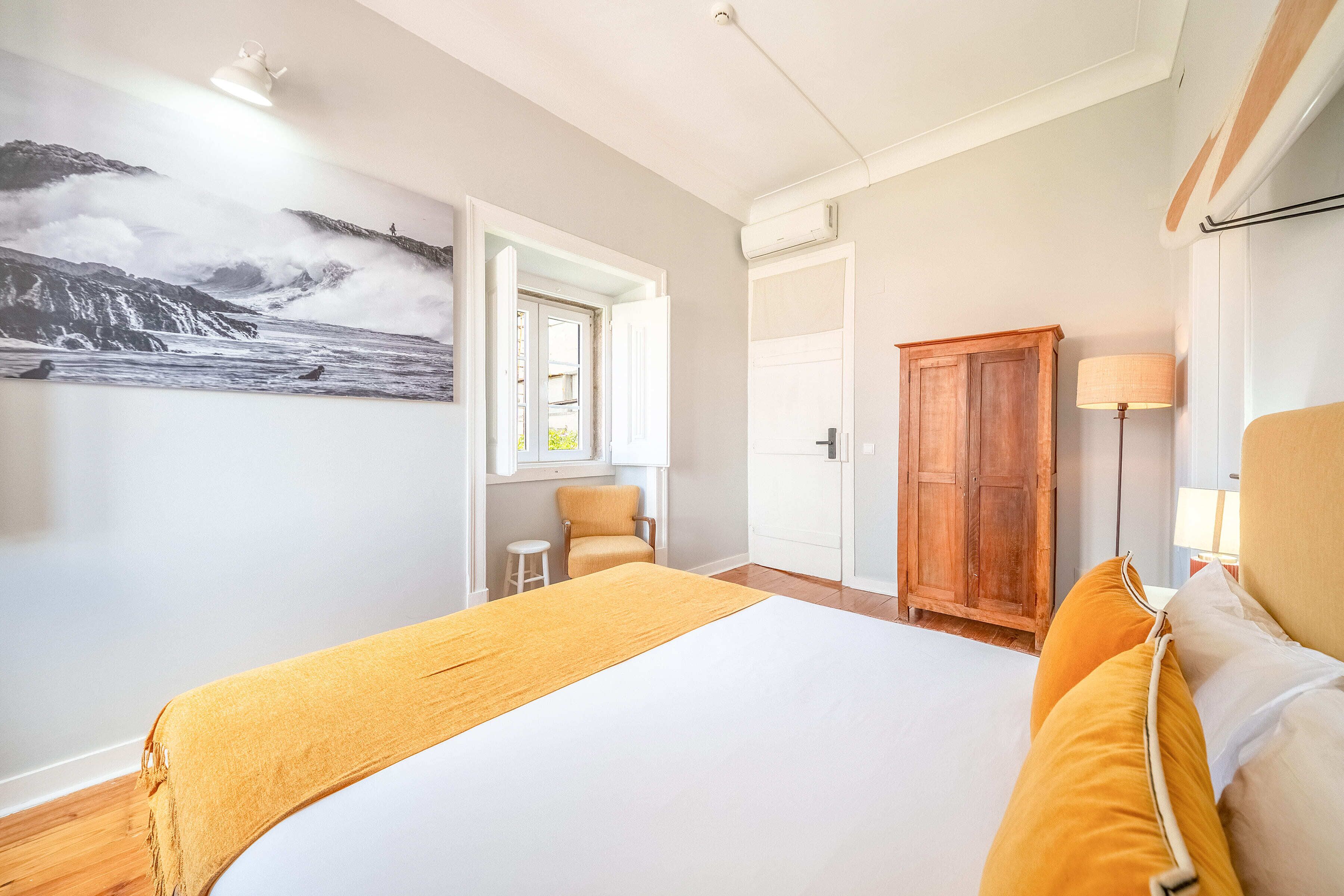Une chambre d’hôtel comprenant un lit, une armoire en bois, une chaise, une petite table et une lampe fixée au mur.