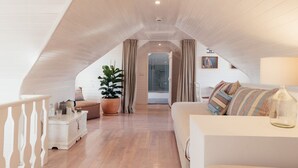 Ein Schlafzimmer im Dachgeschoss mit schrägen Wänden, Holzboden, einem weißen Sofa, einem kleinen Tisch und einer Topfpflanze.