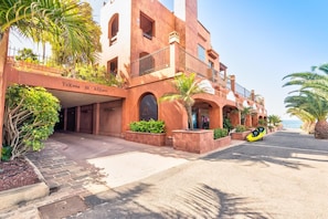 Un hotel con fachada roja, varios balcones y vista al mar.