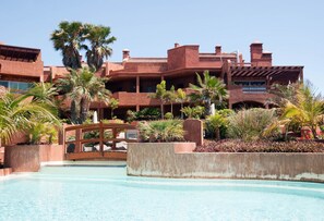 A resort with a swimming pool, palm trees, and a wooden bridge.