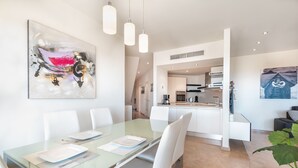 A modern dining area with a glass table, white chairs, and a kitchen in the background. - Bahia - Alzaro 1.3 DELUXE SEA VIEW & JACUZZI 3B (Arona)